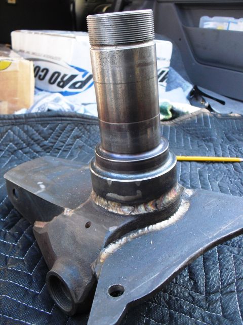 1986 Ford Bronco - A close-up of a metal spindle and bracket assembly, likely a vehicle part, resting on a quilted mat.