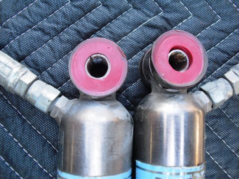 1986 Ford Bronco - Close-up of two Bilstein shock absorbers, likely aftermarket parts, with visible red bushings.