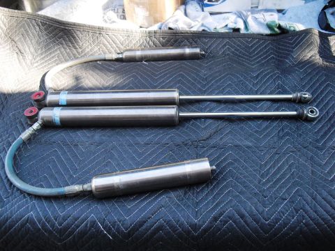 1986 Ford Bronco - Several Bilstein shock absorbers are displayed on a quilted surface, with hoses and mounting hardware visible.