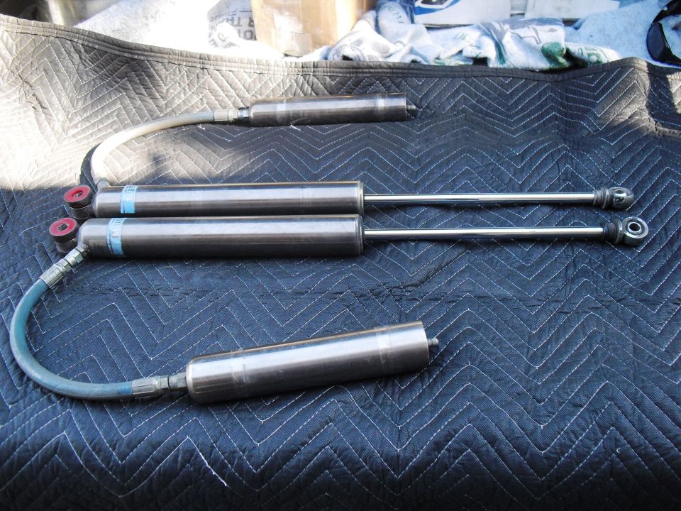 Four Bilstein shock absorbers with external reservoirs laid out on a quilted mat