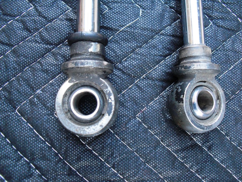Two shock absorber ends with rod ends and bushings, resting on a quilted mat