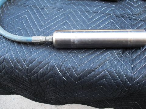 1986 Ford Bronco - A metal shock absorber with a blue hose is placed on a black quilted blanket. The image shows a close-up of the part.