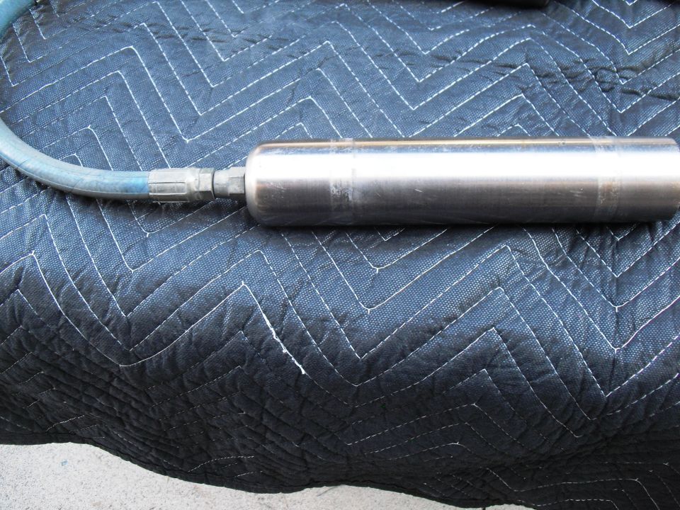 Metal shock absorber with blue hose attached, lying on a black quilted blanket