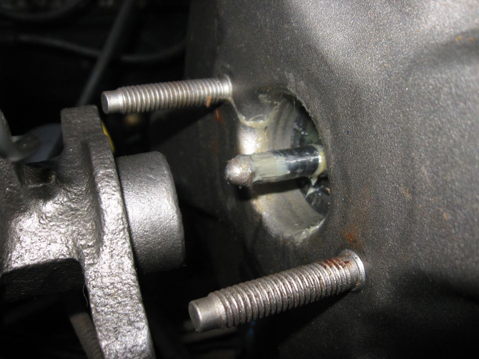 Close-up of a brake booster pushrod with grease, attached to a metal housing with threaded bolts