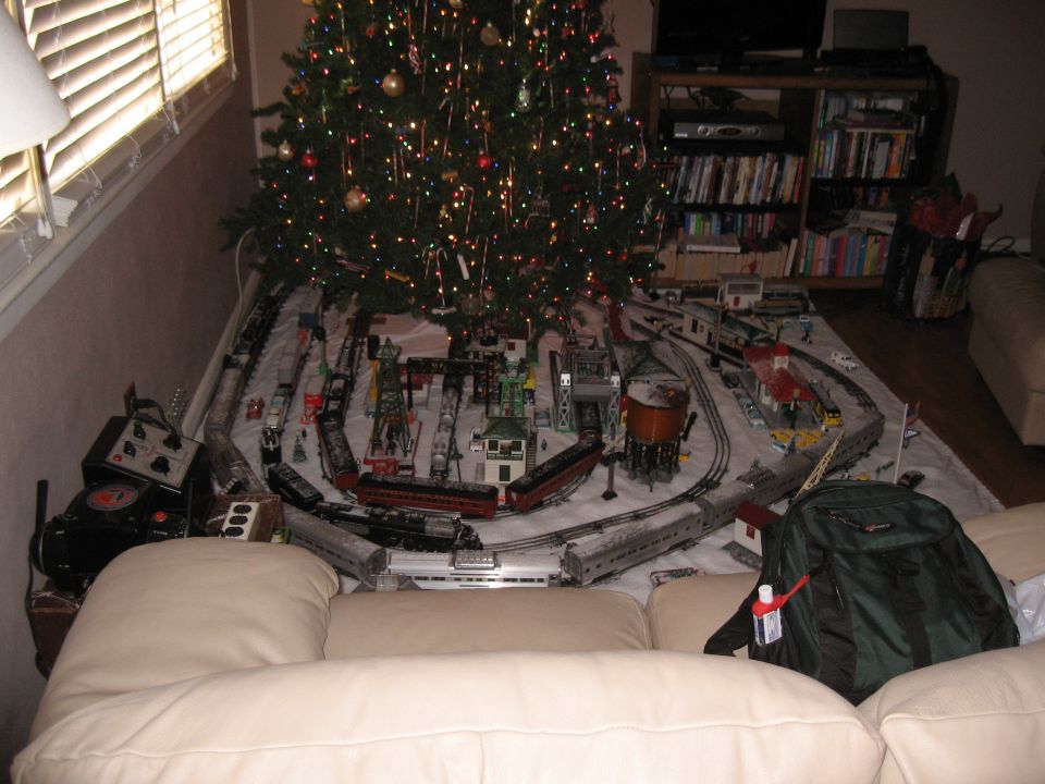 Model train set with multiple trains and buildings arranged around a Christmas tree