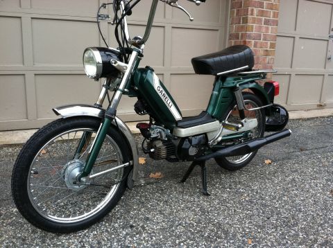 1981 Garelli Rally Sport - A green Garelli moped is shown from a three-quarter front view, parked on an asphalt surface in front of a garage door.