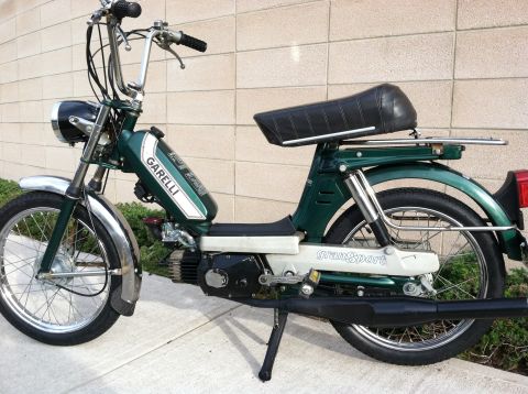 1981 Garelli Rally Sport - A green moped is parked on a sidewalk in front of a brick wall. The moped has chrome accents and visible branding.