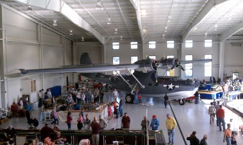 1979 Ford Bronco - A large seaplane is displayed indoors with many people observing it.