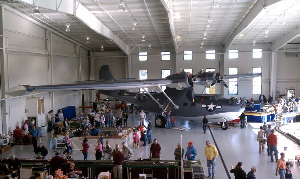 Large seaplane with two engines inside a hangar, people milling around