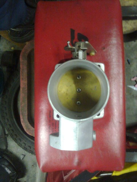 1984 Ford Bronco - A throttle body part is shown resting on a red surface.