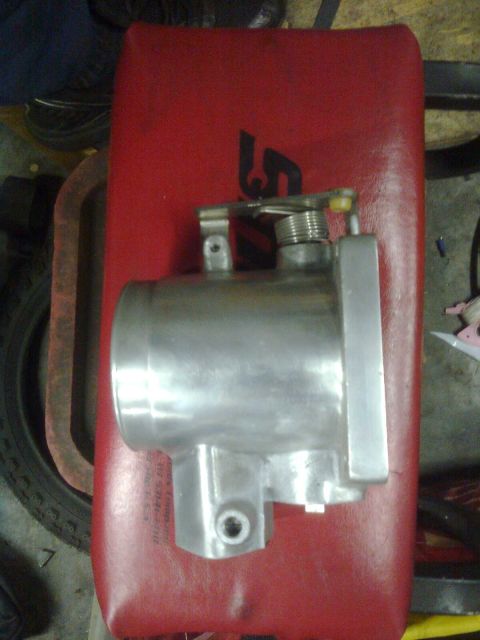1984 Ford Bronco - A metal throttle body sits on a red surface, possibly in a workshop or garage.