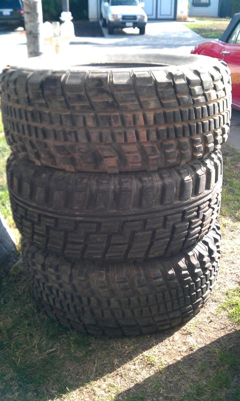 1992 Ford Ranger - A stack of four off-road tires sits on grass, with a white SUV and a red car visible in the background.