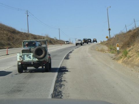 1989 Ford Bronco - A convoy of Jeeps and other vehicles travels down a highway on a clear day.