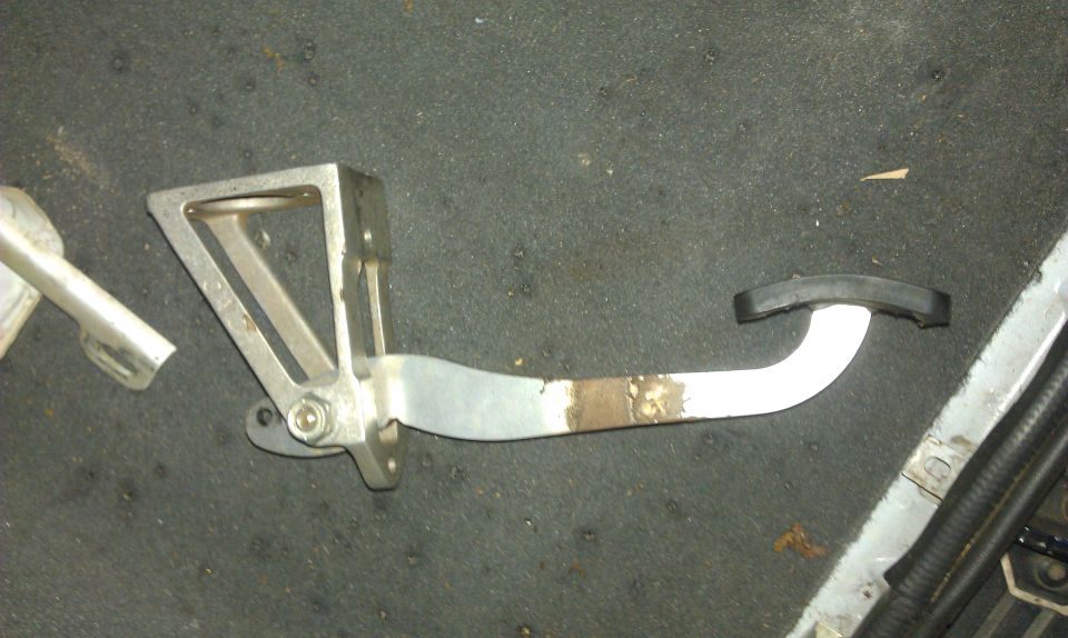 Metal brake pedal assembly with rubber pad, resting on carpeted floor
