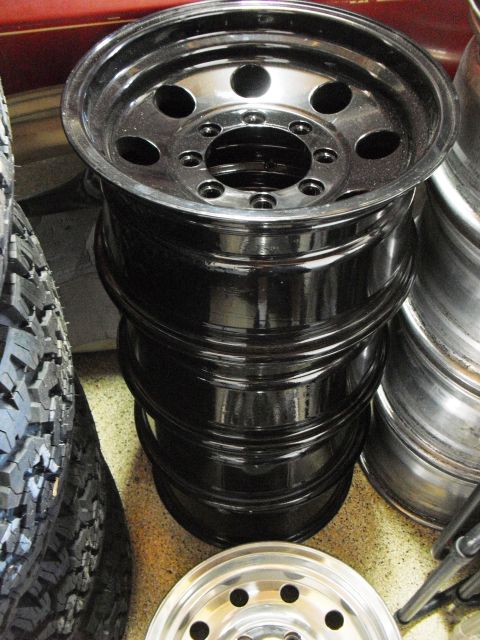 1986 Ford Bronco - Several black rims are stacked on top of each other, with a tire and another rim visible.
