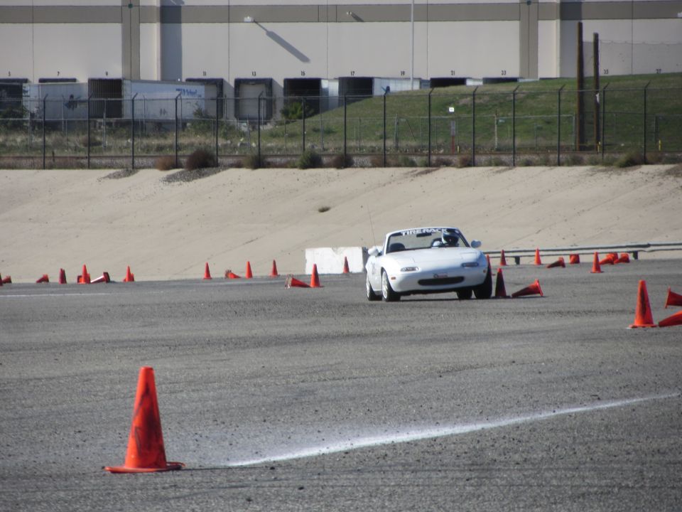 White 1991 Mazda Miata driving on a race track with orange cones