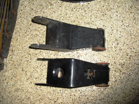 1986 Ford Bronco - Two black leaf spring shackles are shown, one with decorative cross cutouts.