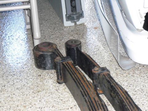 1986 Ford Bronco - Close-up view of rusty leaf springs and shackles, likely from a vehicle's suspension system.