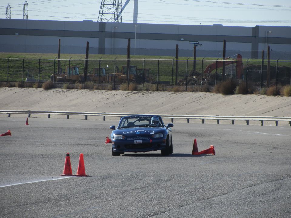 1991 Mazda Miata on a race track with cones, driver wearing helmet
