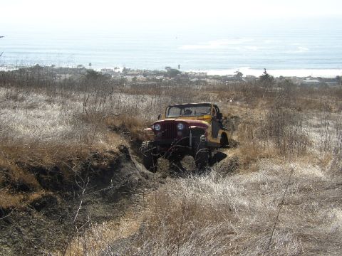 1989 Ford Bronco - Jeep CJ-7 navigates a rough terrain with the ocean visible in the distance.