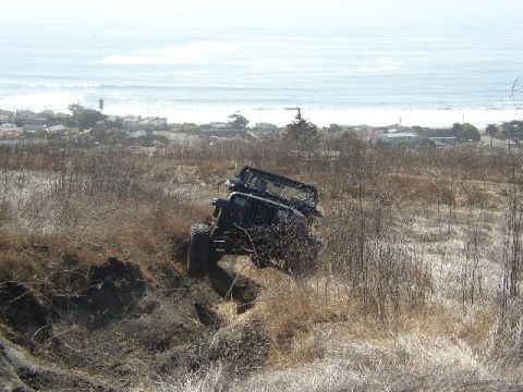 1989 Ford Bronco - A Jeep Wrangler navigates a steep, dry embankment with the ocean in the background.