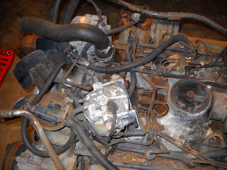 Rusted engine with hoses and electrical connectors. A red tool is visible on the left
