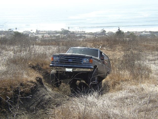 Dark lifted Ford SUV nosed into a dirt ditch with coastal town and ocean behind