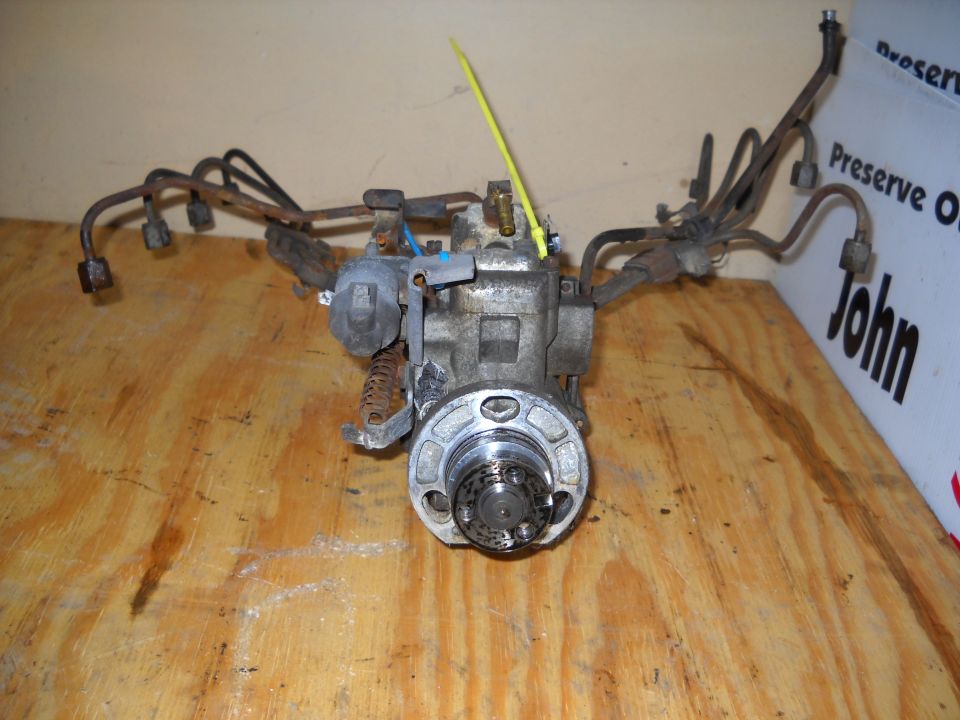 Fuel injection pump with metal lines and a yellow tag, resting on a wooden surface