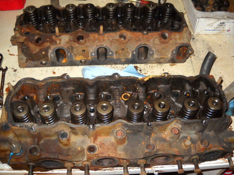 Two rusty engine cylinder heads with valve springs visible, on a workbench