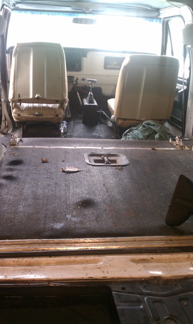 1978 Ford Bronco - The interior of a vehicle is shown, tan front seats and an empty cargo area with a worn floor.