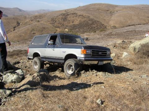 1989 Ford Bronco - A 1989 Ford Bronco navigates a rocky, off-road path under a clear sky.
