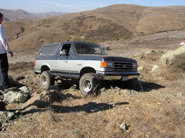 Silver and gray Ford Bronco SUV climbing rocks in dry hills