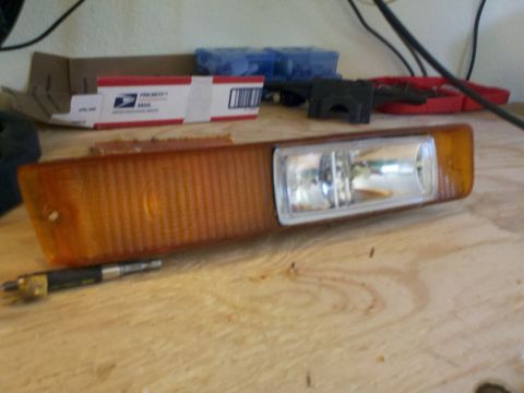 1978 Ford Bronco - A vehicle's amber turn signal assembly is shown resting on a workbench, with various tools and boxes in the background.