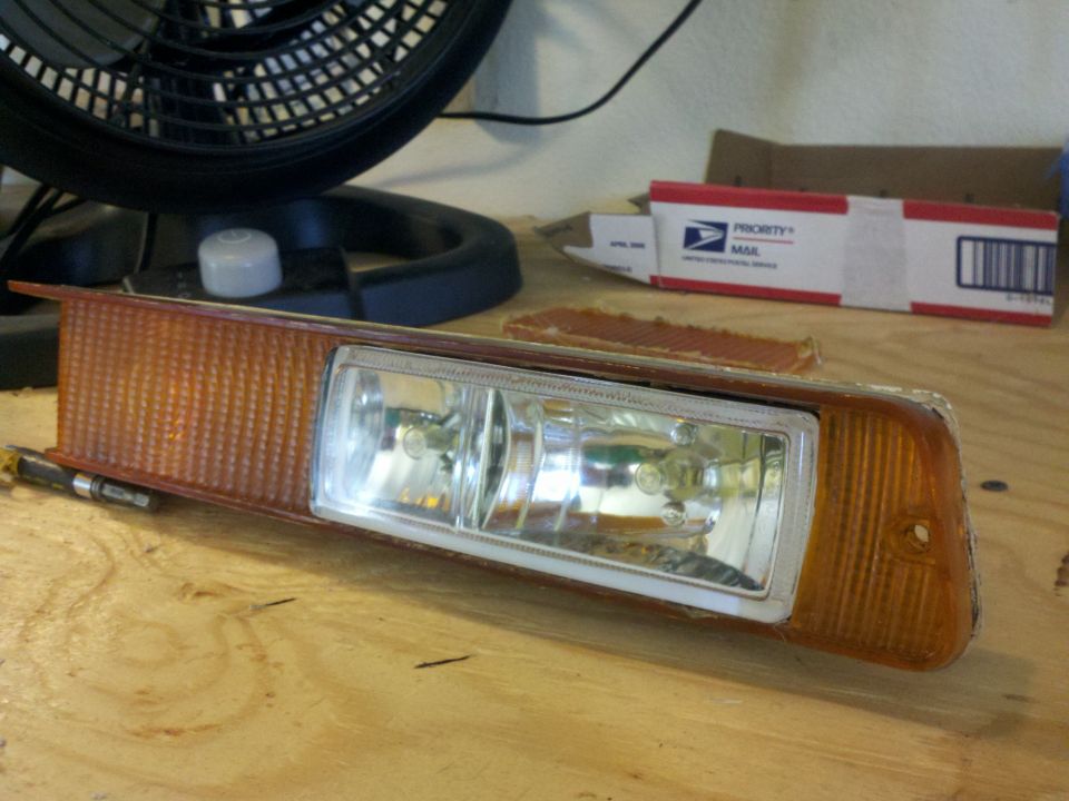 Headlight assembly with amber turn signal and dual bulbs on a wooden surface