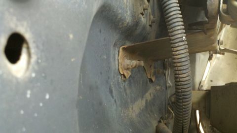 1978 Ford Bronco - Detail of a vehicle's fender liner and a mounting bracket, showing rust and a wire loom.