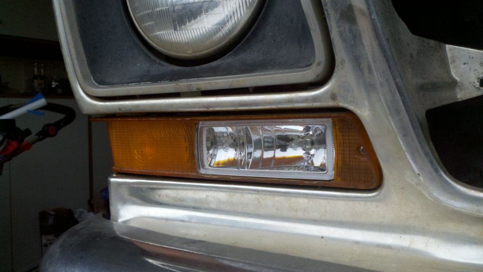 Close-up of a vehicle's front corner, showing the headlight, amber turn signal, and a clear fog light