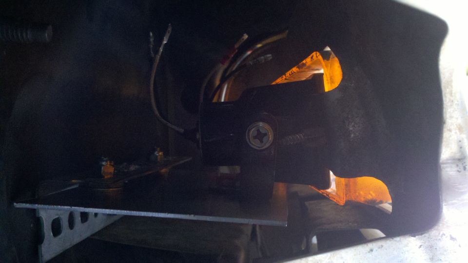 Black fog light assembly with orange reflector and exposed wiring, mounted on a metal bracket