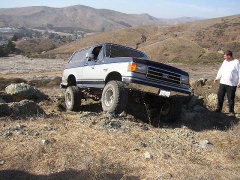 1989 Ford Bronco - A man watches as a lifted Ford Bronco navigates a rocky, off-road terrain.