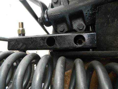 1979 Ford Bronco - Detail of front suspension components, including large coil springs and a black metal bracket with threaded fittings.
