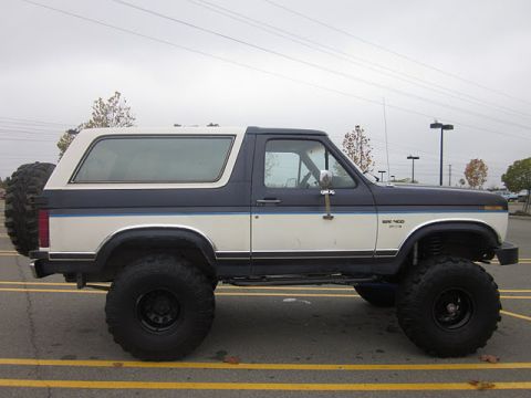 1985 Ford Bronco - Side view of a lifted, two-tone Ford Bronco with a spare tire on the back.