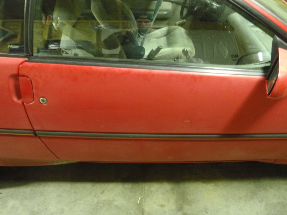 Red coupe passenger door with faded paint and black trim, photographed in a garage