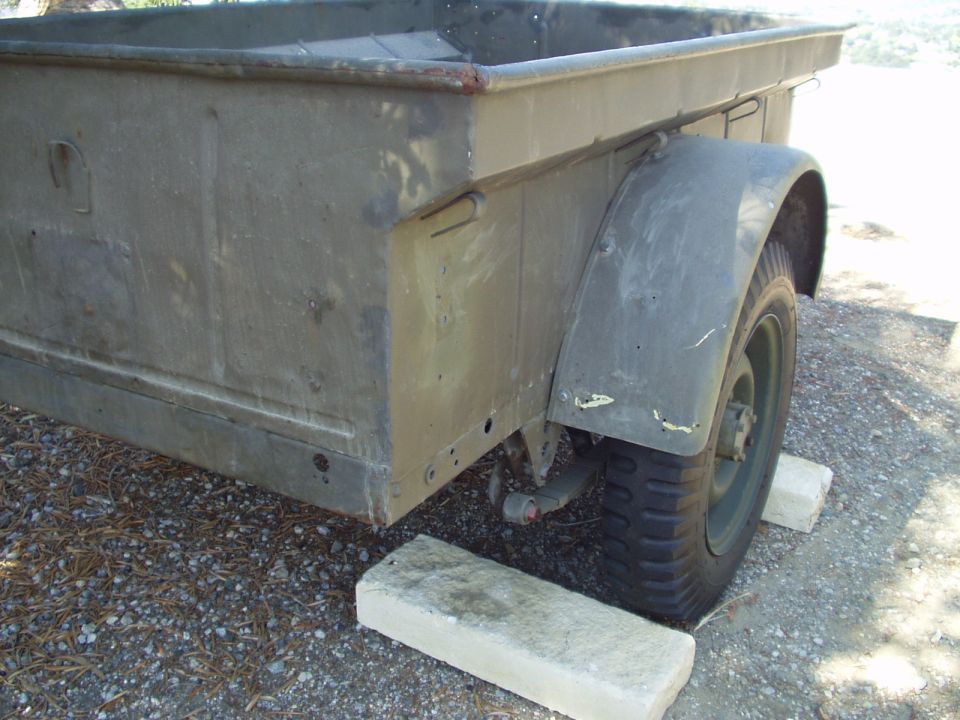 Olive drab military trailer side view, resting on concrete blocks