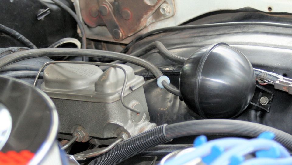 Close-up of car's engine bay showing brake fluid reservoir and a black round vacuum canister