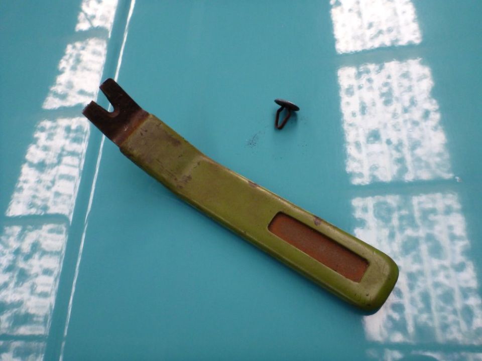 Green trim removal tool and black clip on a blue surface with reflections