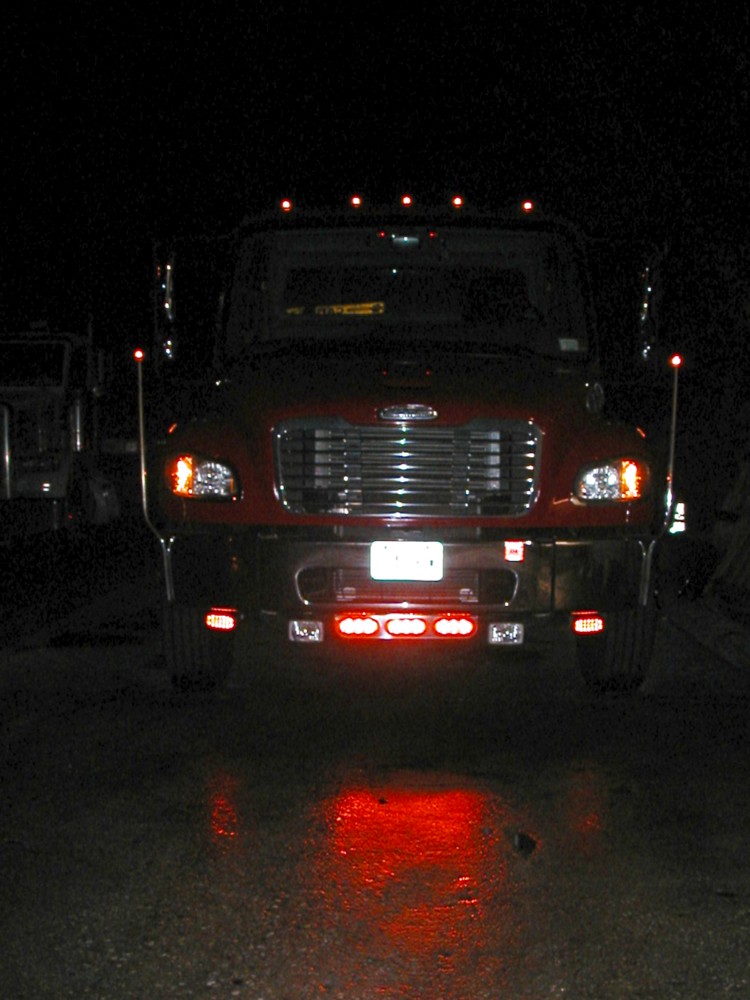 Red Freightliner truck at night with roof marker lights and red bumper strobes lit