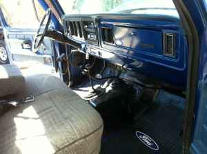 1995 Ford Bronco - The interior of a blue Ford truck features a worn fabric seat and a dashboard with various controls and vents.