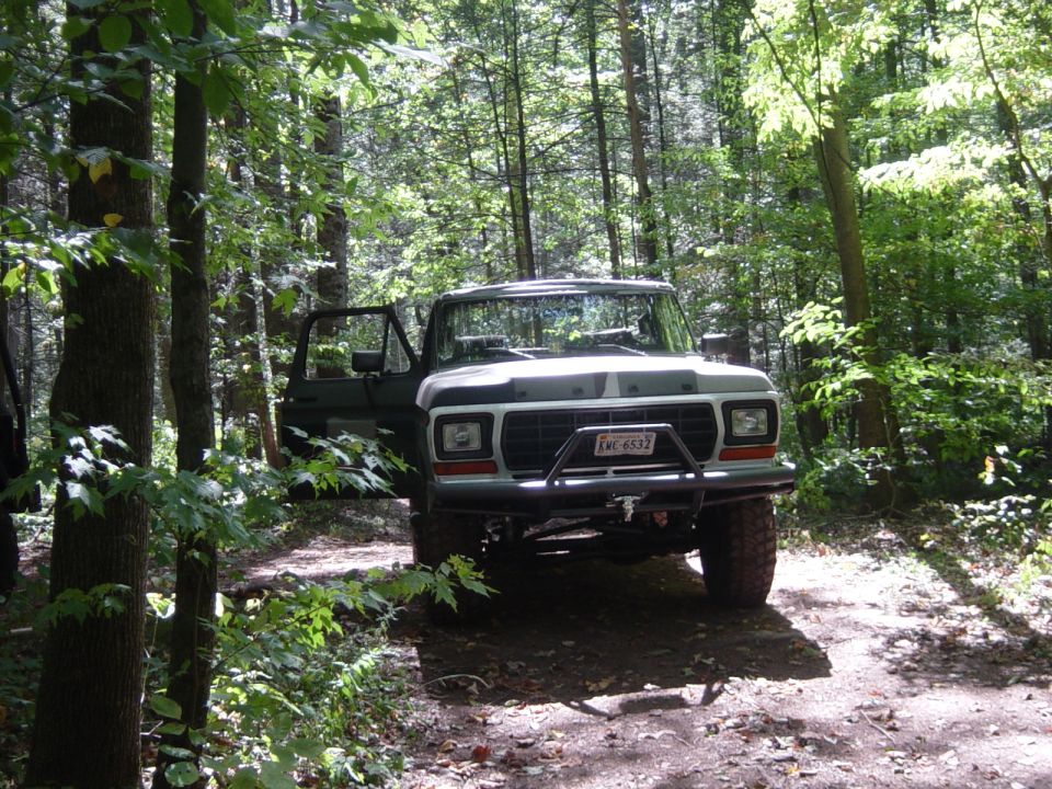 Ford F-Series truck with aftermarket bumper parked on a dirt path in a forest
