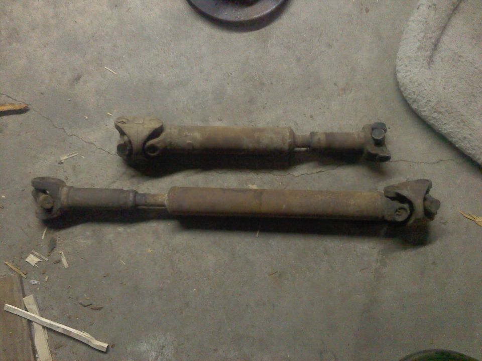Two rusty drive shafts lying on a concrete floor