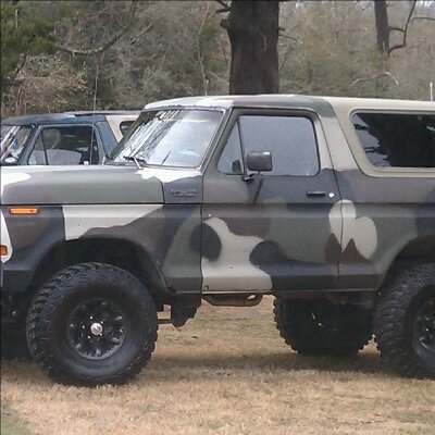 1979 Ford Bronco - A camouflaged Ford Bronco is parked outdoors next to another vehicle.