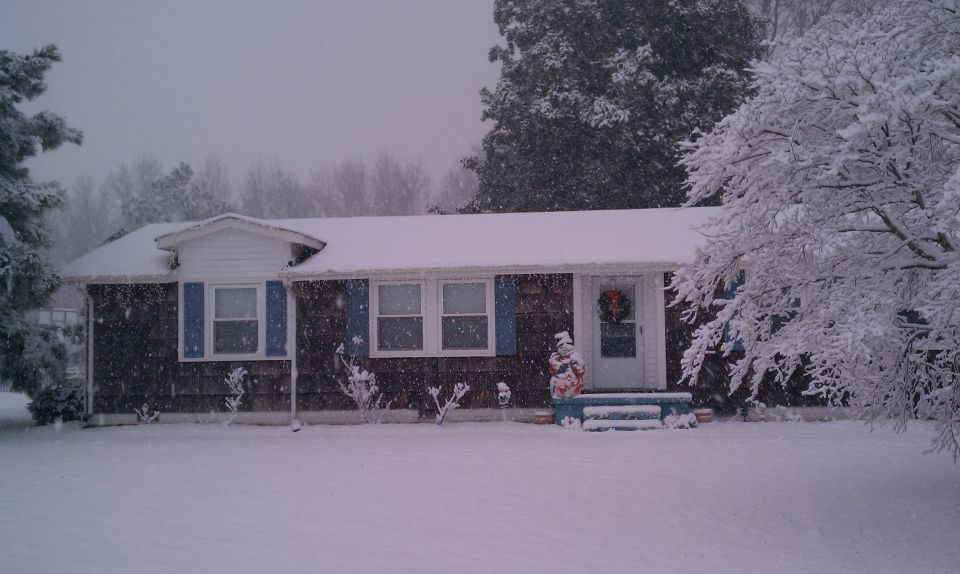 House covered in snow with blue shutters and a wreath on the door